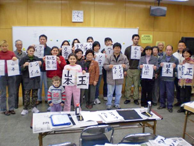 写真:書道体験 学習者が書きあがった半紙を掲げているところ